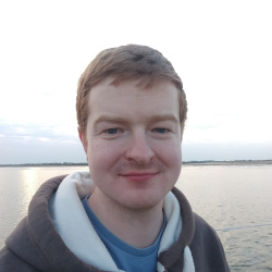 A photo of David, a red-haired man in front of the sea.